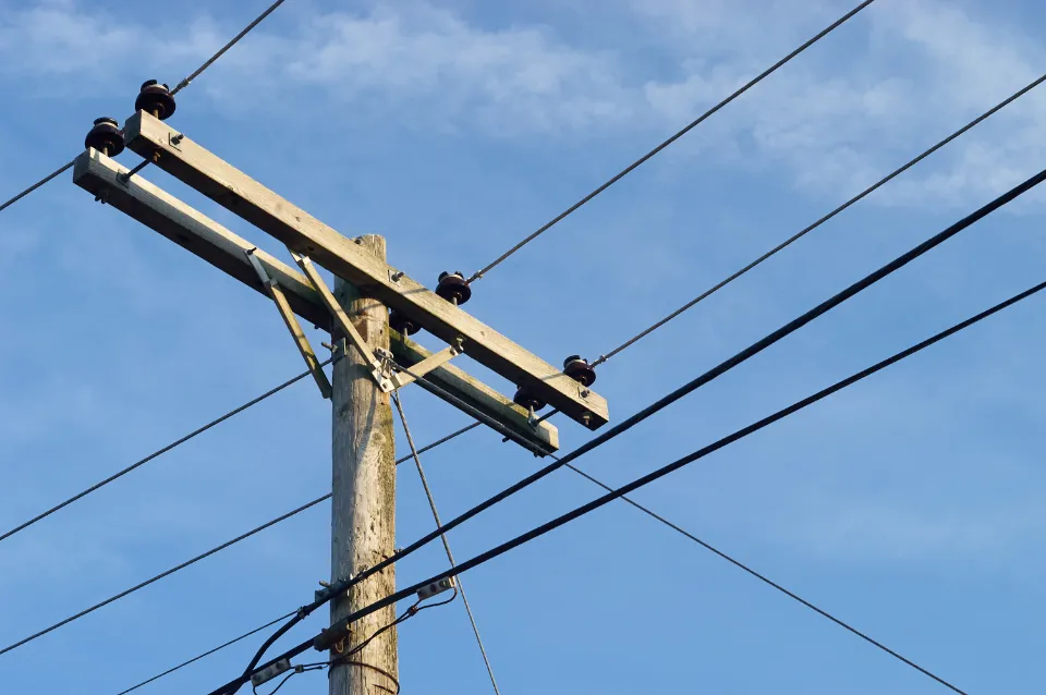 Wooden utility pole carrying local distribution lines against a blue sky